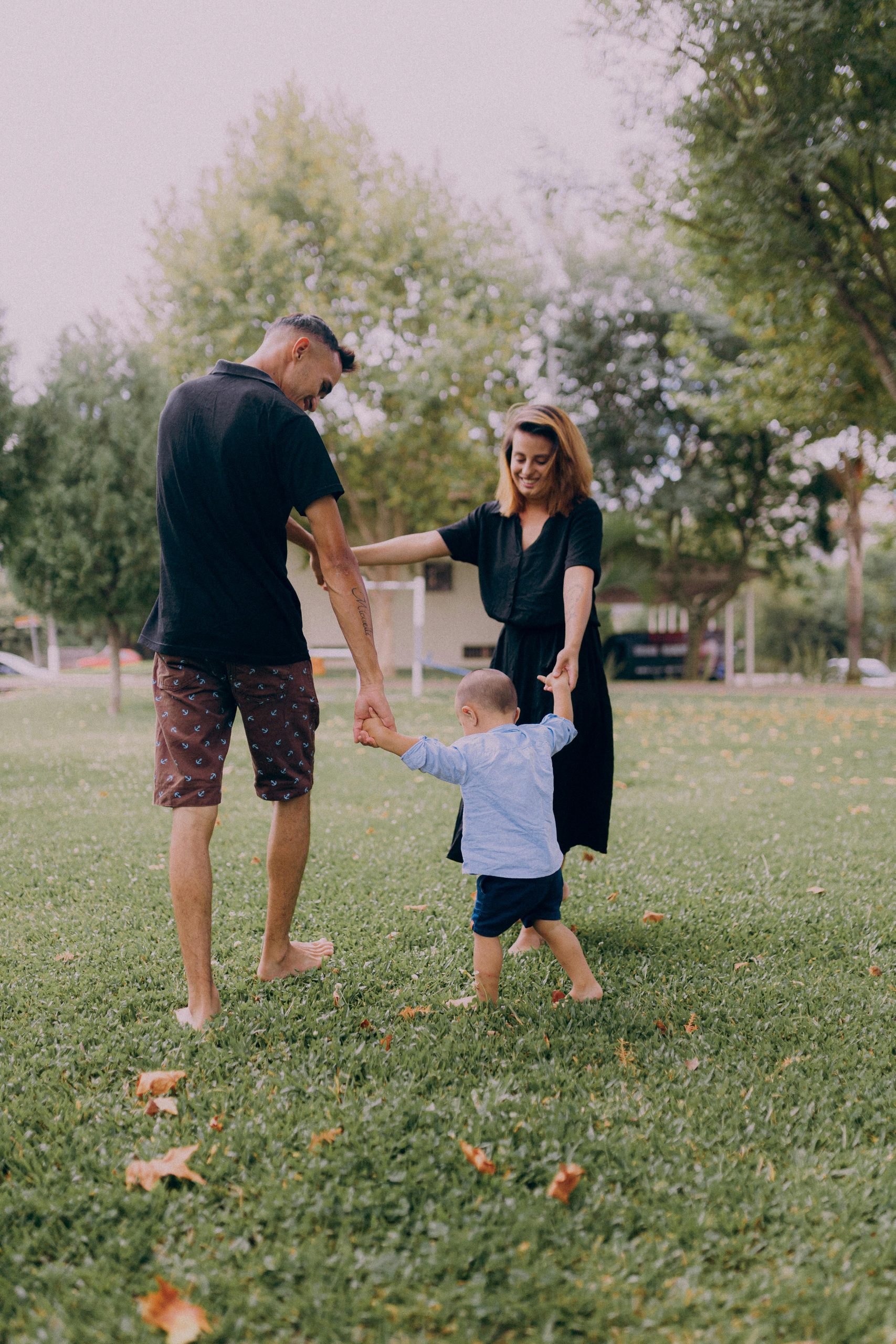 Parents enjoying playtime with their child in a sunny park setting.