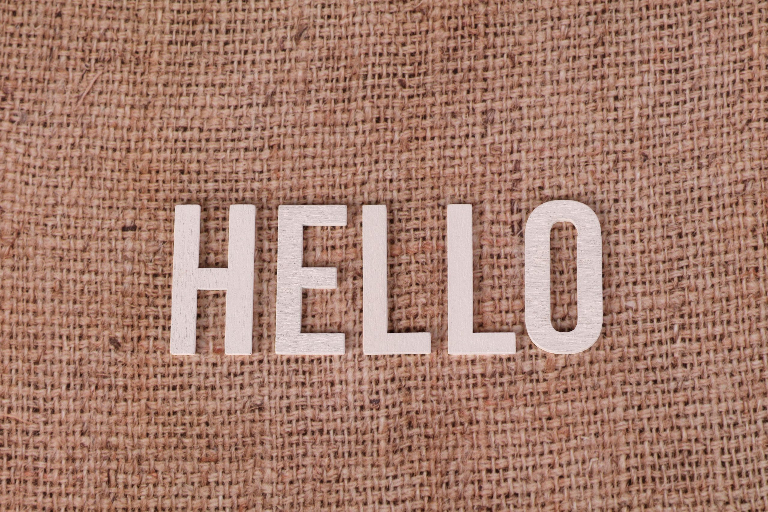 Wooden letters form the word 'HELLO' on a rustic burlap background, offering warm greetings.
