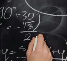 Hand writing complex math equations on a blackboard in a classroom setting.